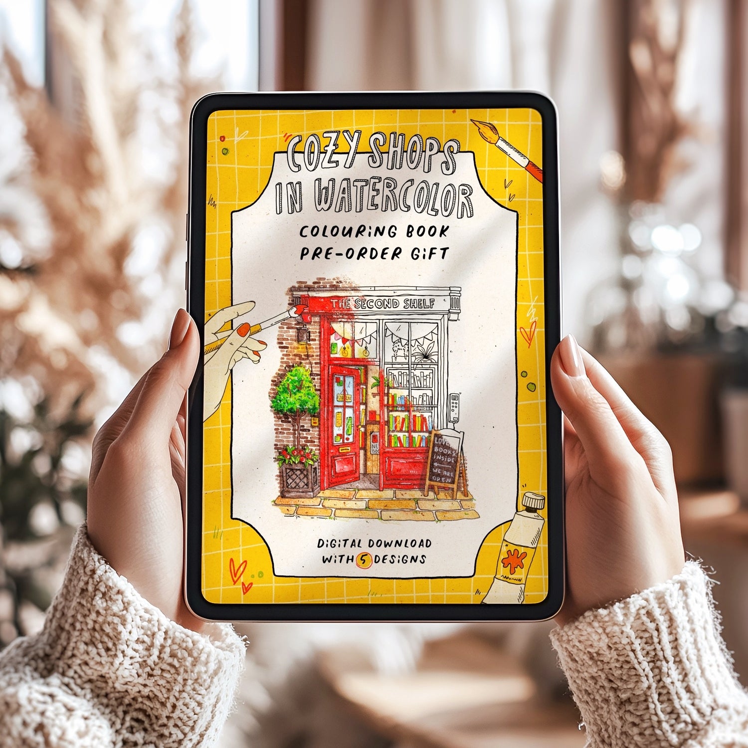 Person holding a tablet with a Cozy Shops in Watercolor coloring book pre-order gift on the screen.
