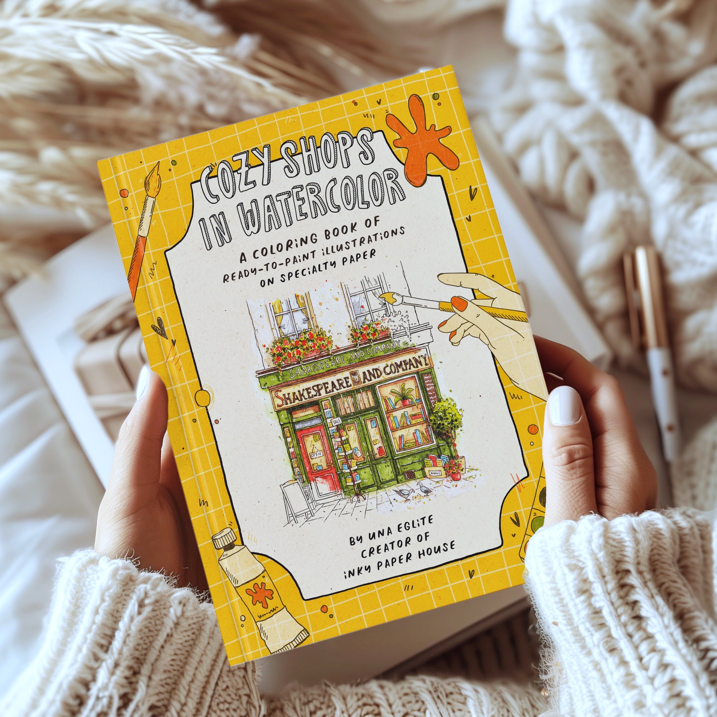 Coloring book titled 'Cozy Shops in Watercolor' held by a person with a cozy background.