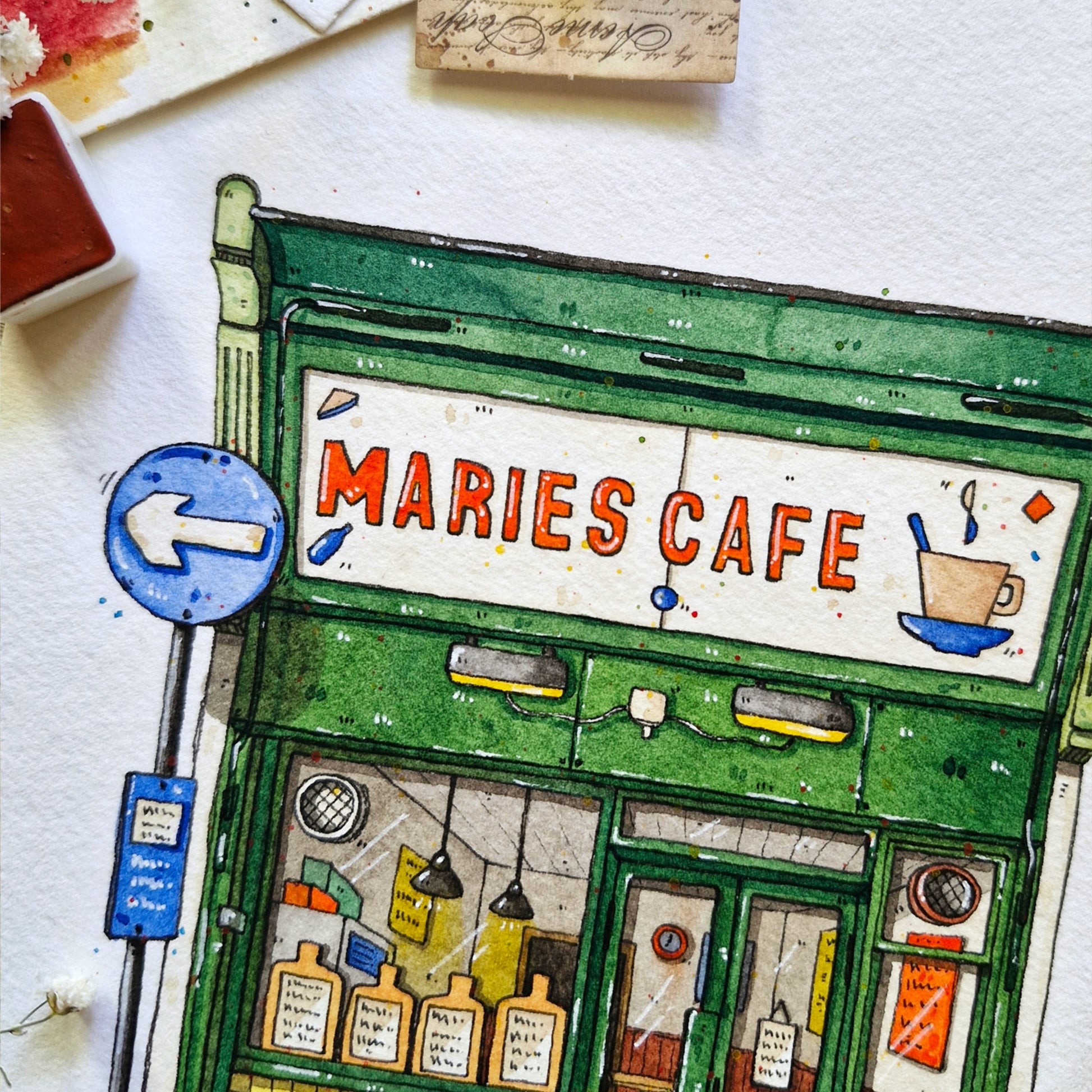Illustration of a cafe named 'Maries Cafe' with a green facade and colorful sign.