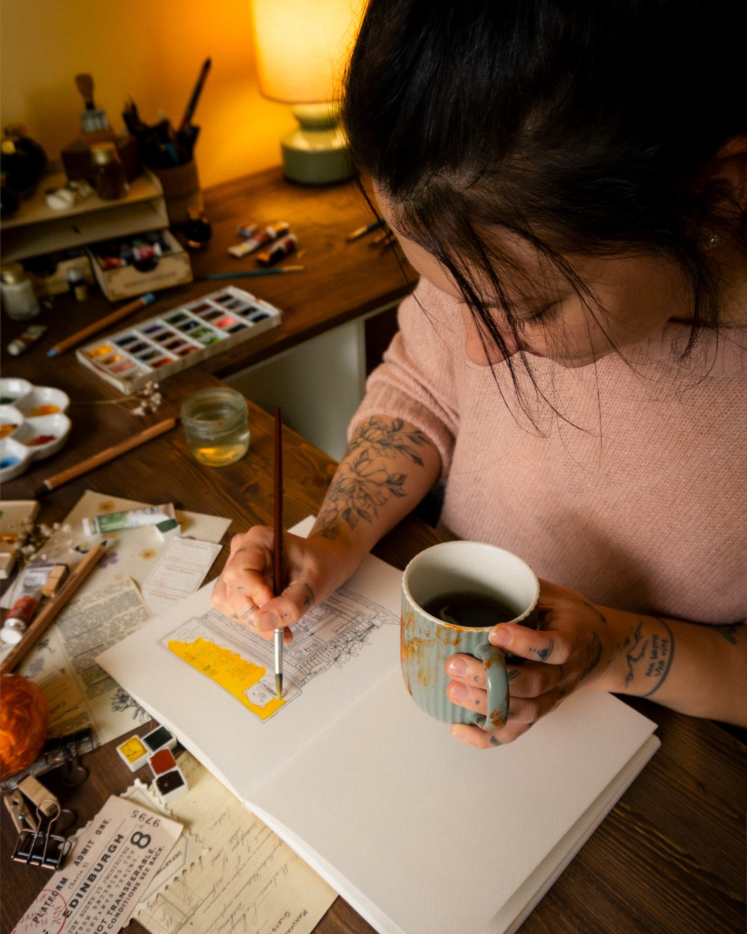 Person with tattoos holding a mug and painting in a studio setting