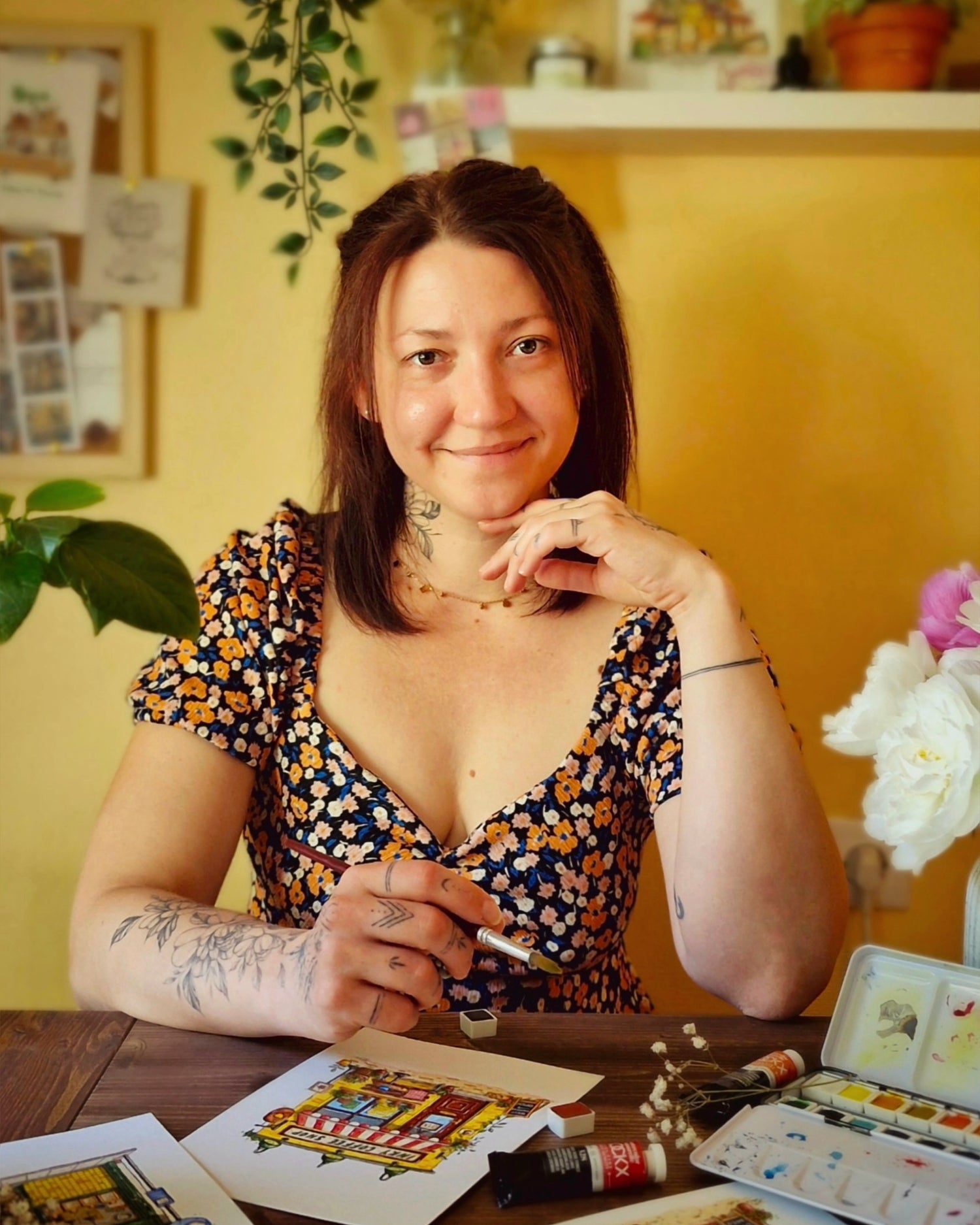 Woman sitting at a table with art supplies, smiling in a casual setting.