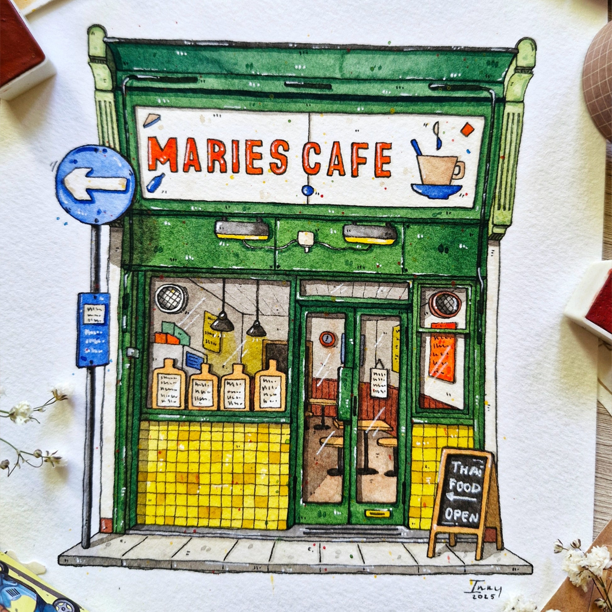 watercolor and ink Illustration of a cafe named 'Maries Cafe' with a green facade and yellow tiles.