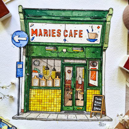 watercolor and ink Illustration of a cafe named 'Maries Cafe' with a green facade and yellow tiles.